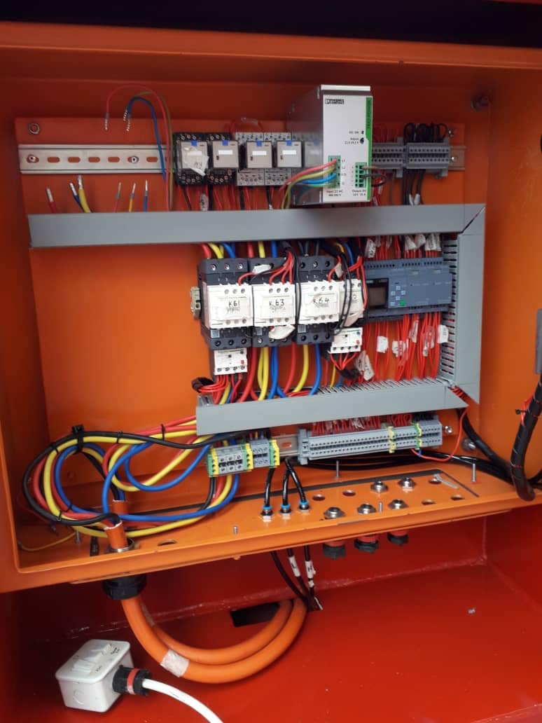 Electrical control components and neatly arranged wiring inside an orange cabinet